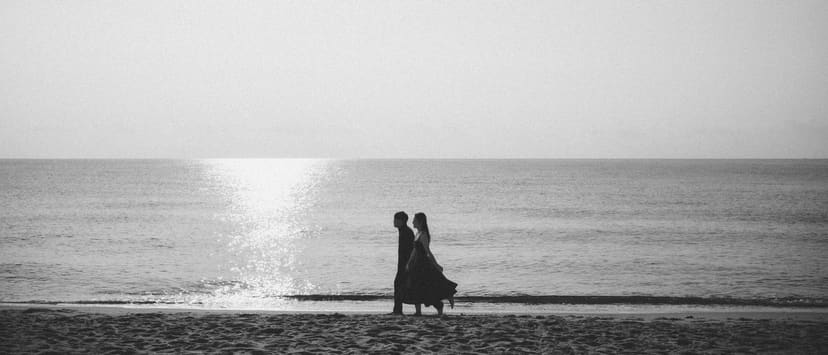 A long black-and-white band: two silhouettes on a path of sun on water